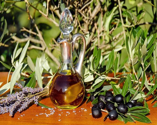 A variety of fresh vegetables and olive oil on a wooden kitchen table representing wholesome cooking